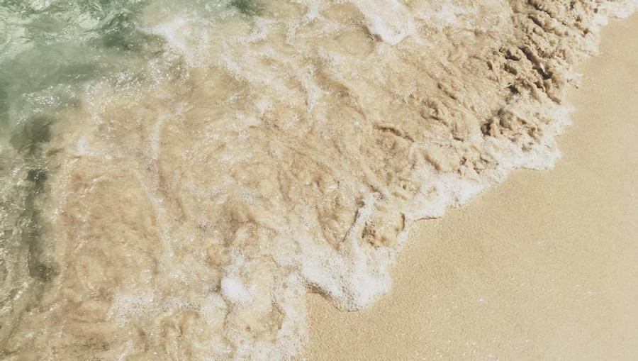 A downward view of crystal-clear water washing up on the sand in Grenada.