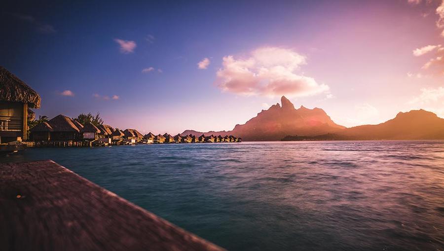 A view of a sunset at the beach with overwater bungalows. 