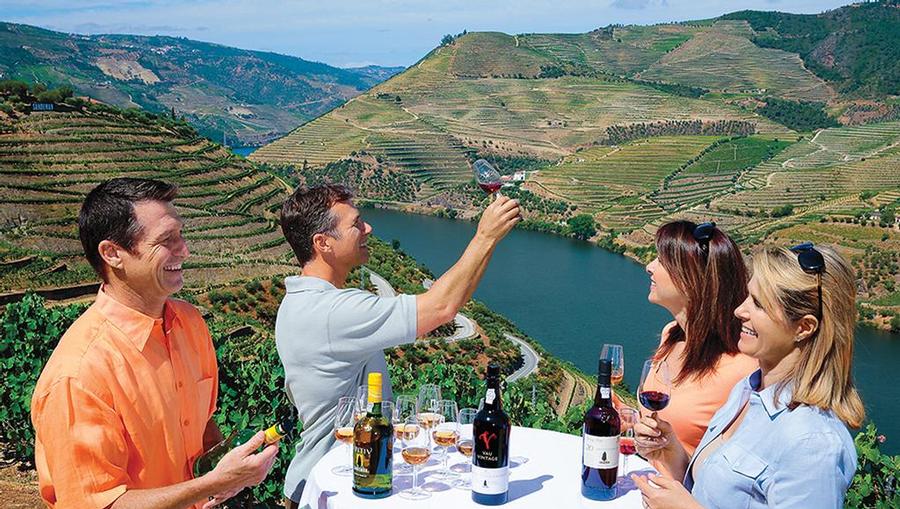 Two couples enjoying wine with a valley and river view.