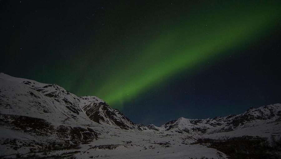Aurora Borealis shining a green beam of light over the Alaskan mountain scape.