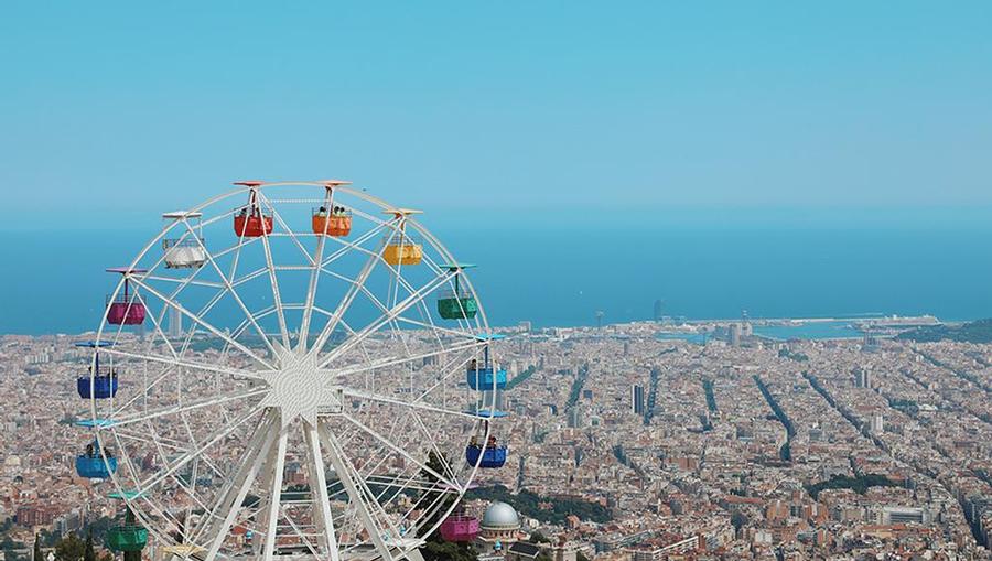 A wide view of the big wheel of Barcelona in Tibidabo Amusement Park, with a beautiful view of the shoreline behind it.