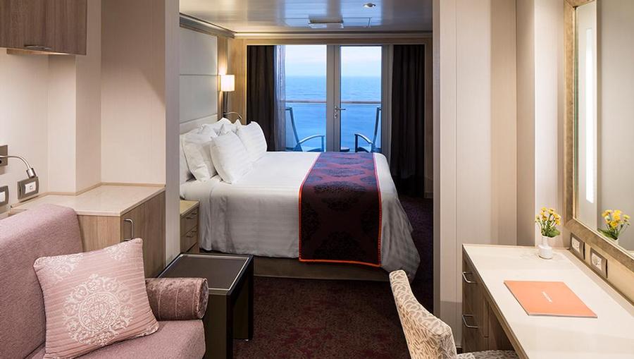 An inside view of the Vista Suite bed, extra seating area, desk, and balcony with a beautiful view.
